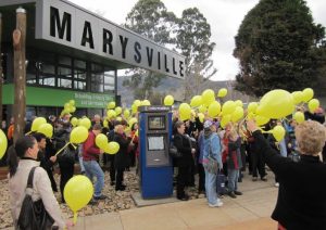 Marysville residents holding yellow balloons gathered around an information kiosk